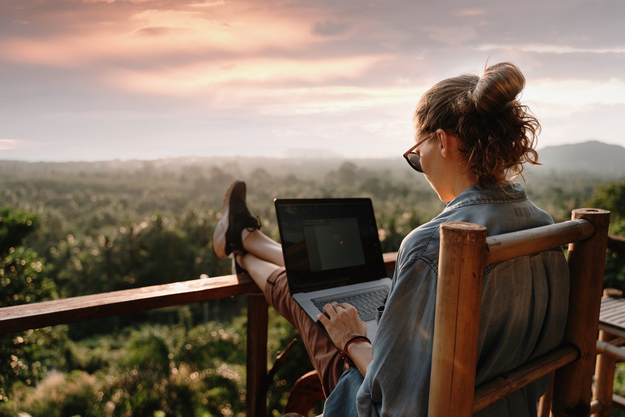 Junges Mädchen arbeitet an einem Laptop bei Sonnenuntergang im Hintergrund sind die Tropen zu sehen
